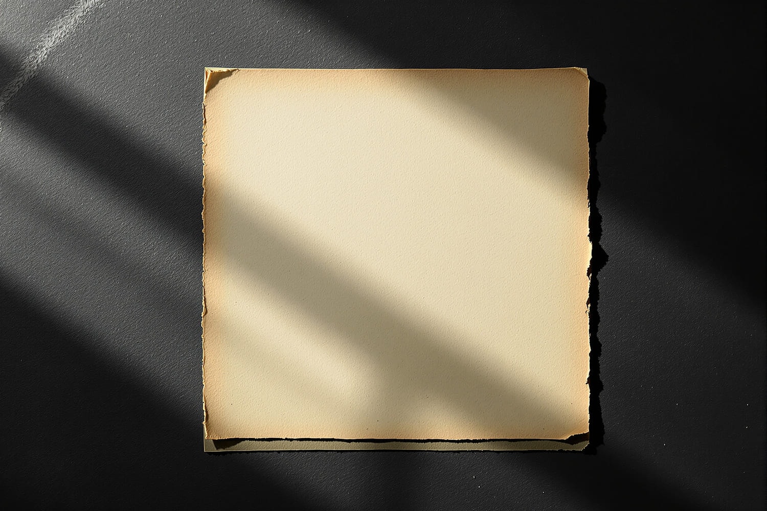 A single blank sheet of paper on dark slate, lit from two directions so that it casts two different shadows